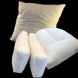 Pile of cushions and pillows. Large square cushion at the back with two rectangular pillows and one baffled cushion at front on left.