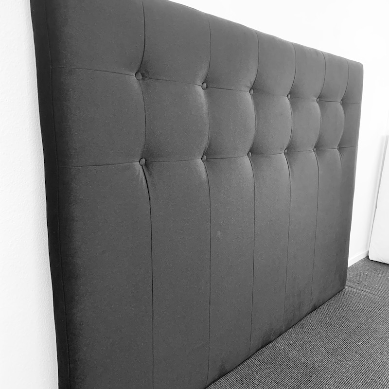 Button headboard in grey upholstery leaning against white wall