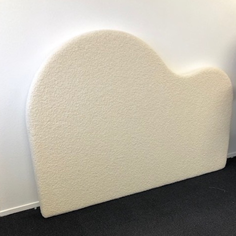 Curved headboard in wool upholstery leaning against white wall on grey carpet